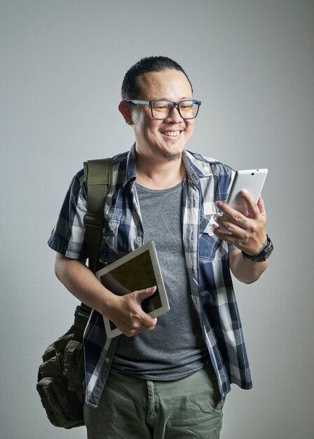 Hombre asiático sonriente sosteniendo un teléfono inteligente y una mesa digital