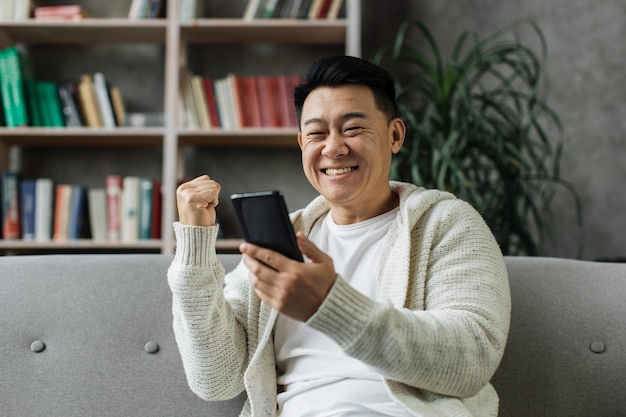 Hombre asiático sorprendido leyendo buenas noticias en un teléfono inteligente moderno