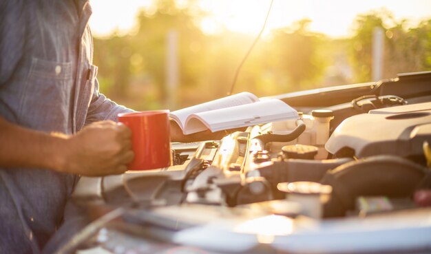 Hombre asiático sosteniendo y leyendo el manual del usuario del coche para comprobar el motor del coche moderno