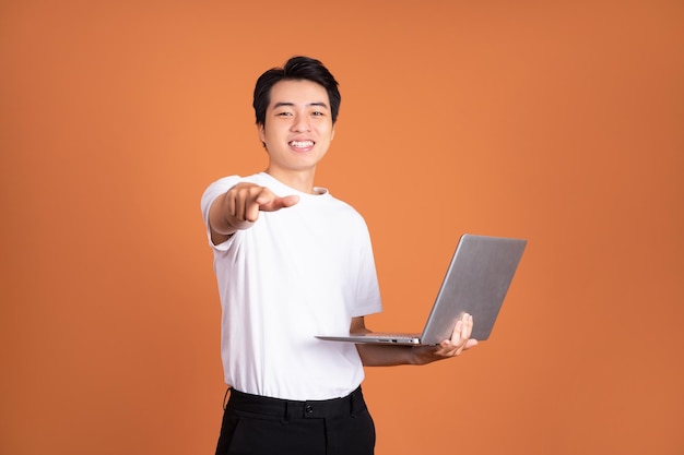 Hombre asiático sosteniendo portátil aislado sobre fondo naranja