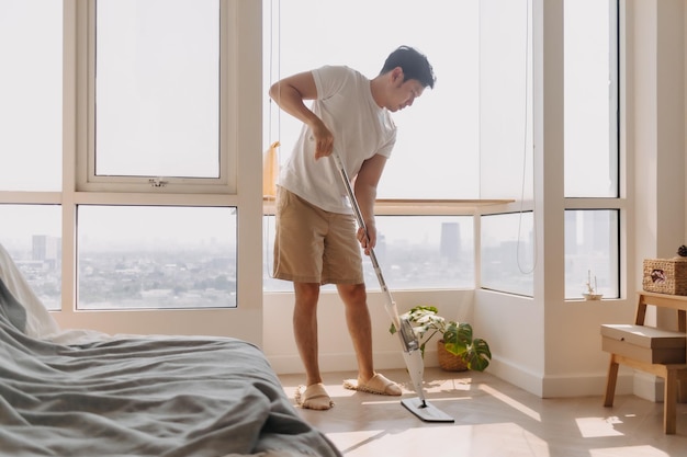 Hombre asiático tailandés usando una mopa para limpiar el suelo en el apartamento de la sala de estar Hombre haciendo tareas domésticas