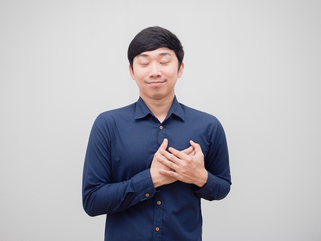 Hombre asiático toca su corazón con la mano con la cara feliz cerca de los ojos loveelf concepto fondo blanco.