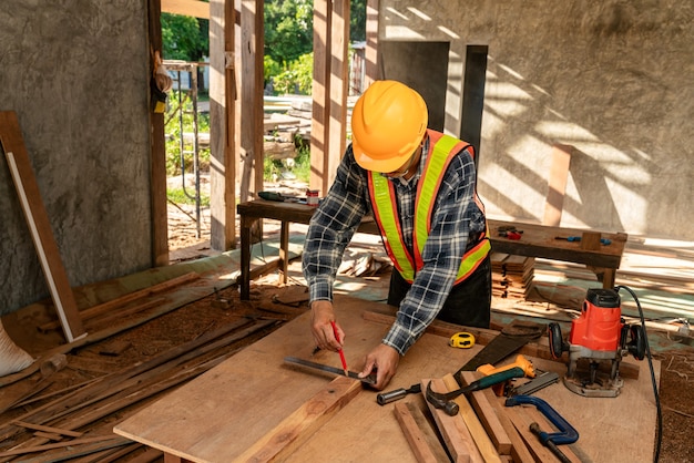 Hombre asiático trabaja en un taller de carpintería. Carpintero trabajando con equipo en la mesa de madera en el sitio de construcción.