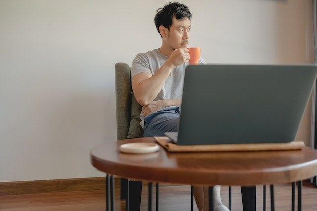 Foto hombre asiático está trabajando con su computadora portátil y tomando café.