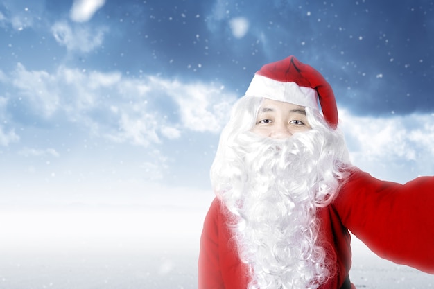 Hombre asiático en traje de Santa tomando un selfie con una nevada. Feliz Navidad