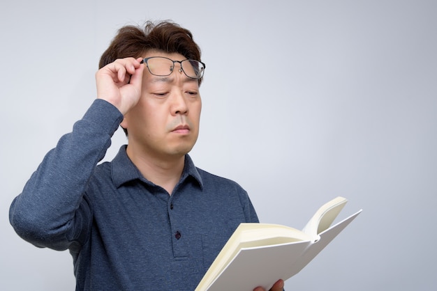 Hombre asiático tratando de leer algo en su libro. mala vista, presbicia, miopía.