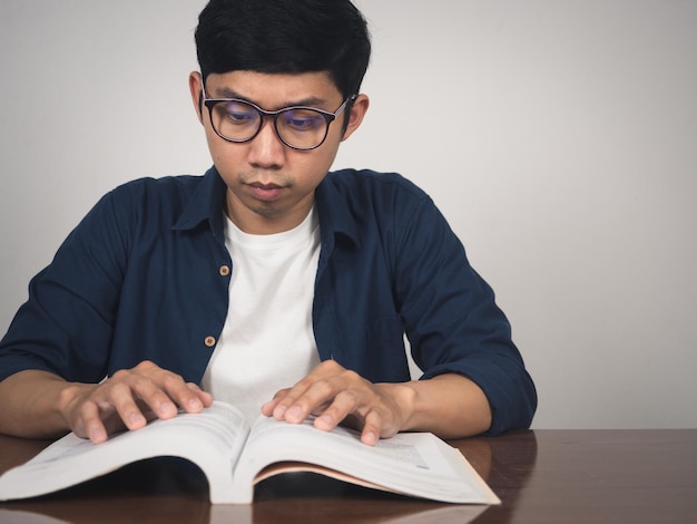 El hombre asiático usa anteojos aprendiendo un libro de texto sobre la mesa