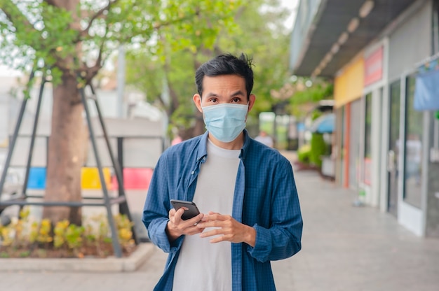 Hombre asiático usar máscara médica con smartphone caminando en la calle