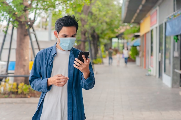 Hombre asiático usar máscara médica con smartphone caminando en la calle