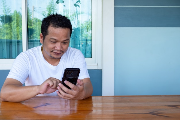 Hombre asiático vestido con camisa blanca con el teléfono en una mesa de madera