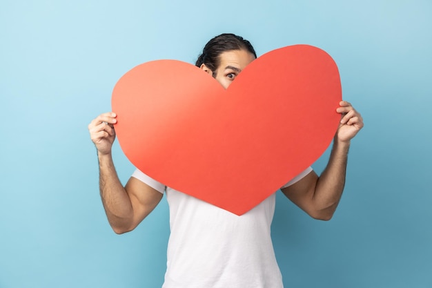 Hombre asomándose de un gran corazón de lectura con una mirada coqueta y expresando un saludo de amor en el día de San Valentín