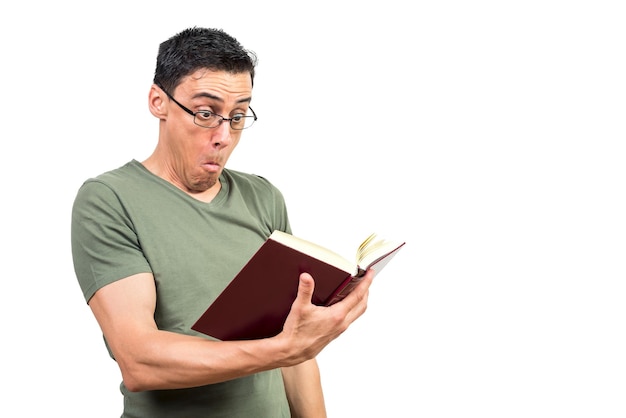 Hombre asombrado con camiseta verde y anteojos leyendo un libro impactante mientras está de pie contra el fondo blanco