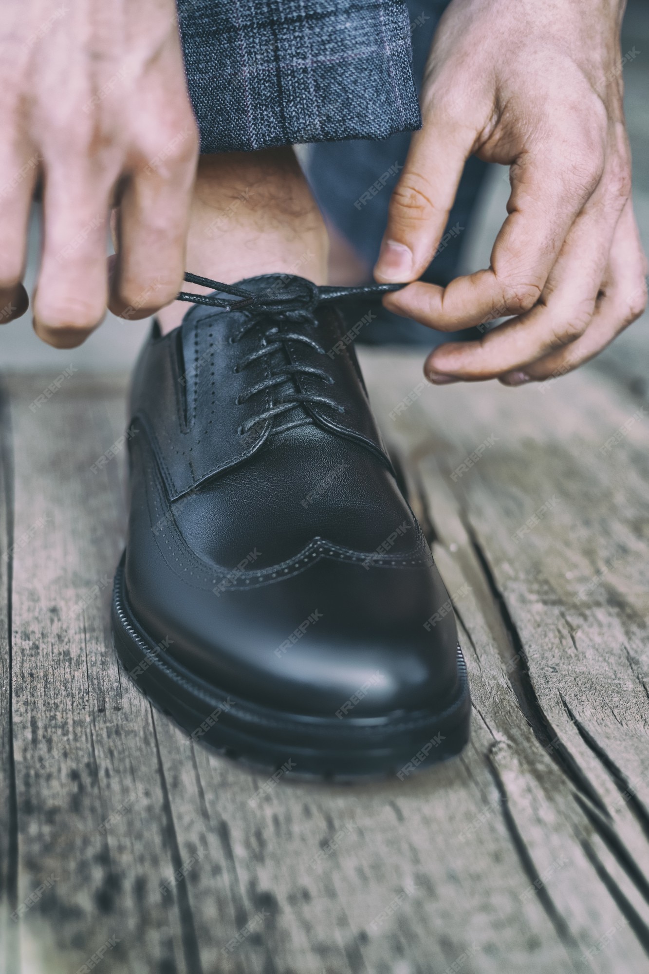 El hombre ata sus cordones en los zapatos de charol negro sobre un piso de madera vieja, de tonos | Foto Premium