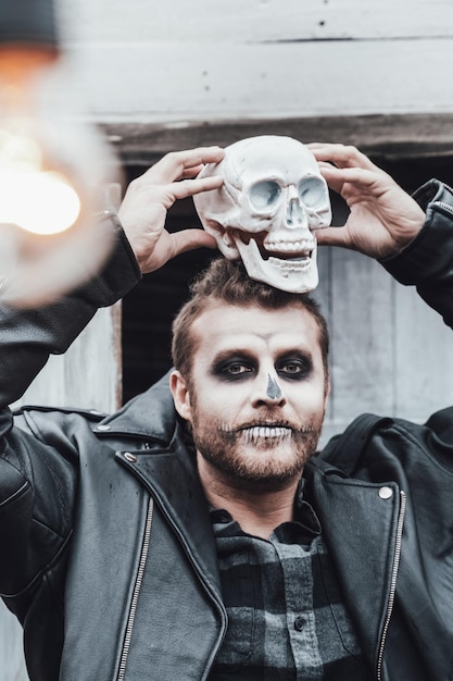 Hombre aterrador con rastas mirando el cráneo Celebrando Halloween Aterrador maquillaje de monstruo de cara blanca negra y elegante imagen de disfracesHorrorfun en la fiesta infantil en el granero en streetShirtjackets