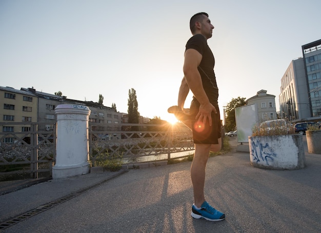 hombre atleta calentando y estirando mientras se prepara para correr en la calle de la ciudad en la mañana soleada