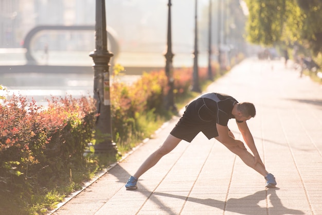 Foto hombre atleta calentando y estirando mientras se prepara para correr en la calle de la ciudad en la mañana soleada