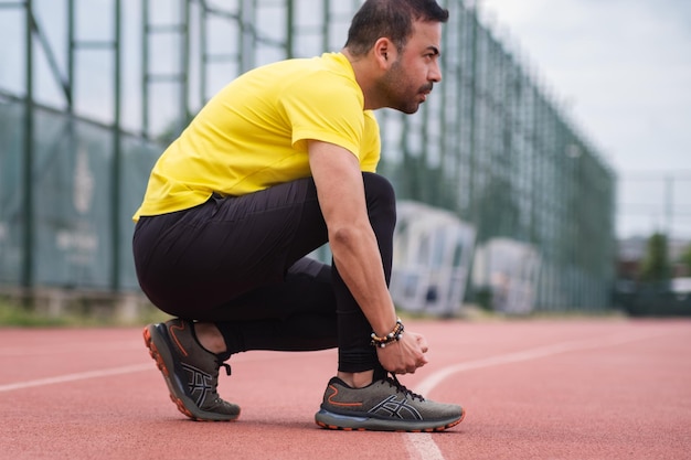 Hombre atleta en calzado deportivo tomando un respiro en cuclillas sobre la pista de atletismo de goma