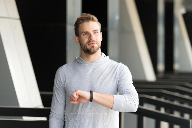 Hombre atleta en la cara satisfecha comprobando el tiempo de fondo urbano Atleta con cerdas con rastreador de fitness o podómetro terminado a tiempo Deportista entrenando con podómetro Concepto justo a tiempo