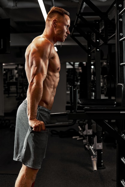 El hombre un atleta se dedica a un gimnasio, haciendo un ejercicio sobre los músculos de los brazos bíceps fondo negro. Foto de alta calidad.