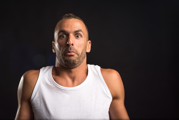 Hombre atleta dudoso en camiseta sin mangas. De cerca. Fondo negro.