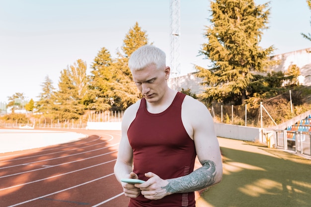 Hombre atleta en pista de atletismo, mirando su smarpthone