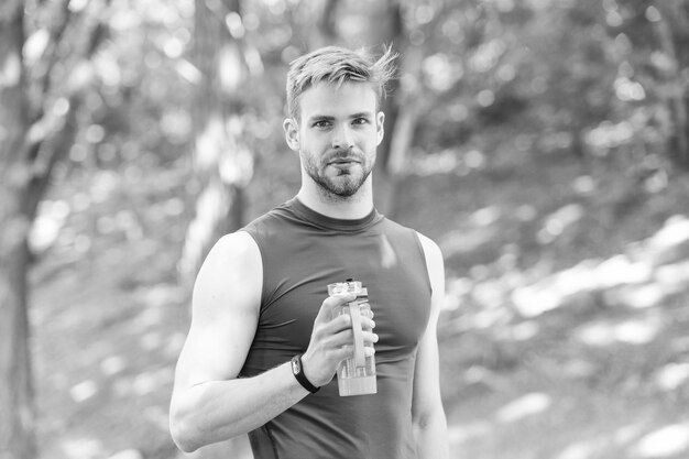 Hombre atleta sostiene botella cuidado hidratación cuerpo después del entrenamiento Refrescante bebida vitamínica después de un gran entrenamiento Atleta bebe agua después de entrenar en el parque Hombre apariencia atlética sostiene una botella de agua