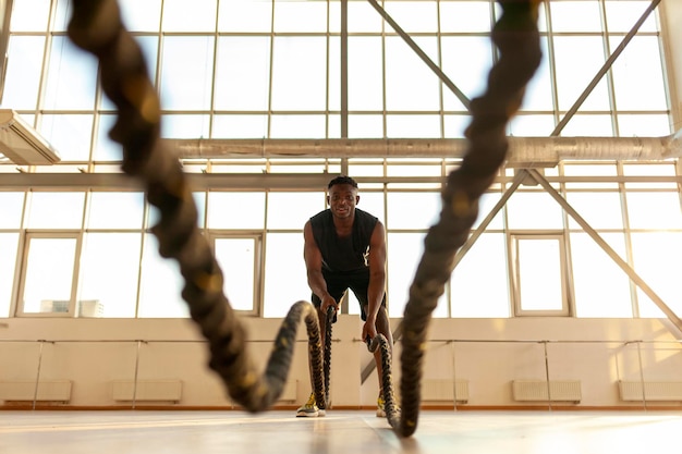 hombre atlético afroamericano en ropa deportiva entrenando en el gimnasio y agitando las cuerdas