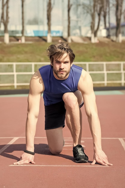 Hombre atlético barbudo con cuerpo musculoso que se extiende en la pista de atletismo