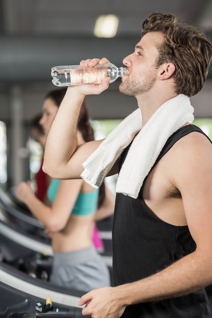 Hombre atlético bebiendo agua mientras se ejecuta en la cinta en el gimnasio