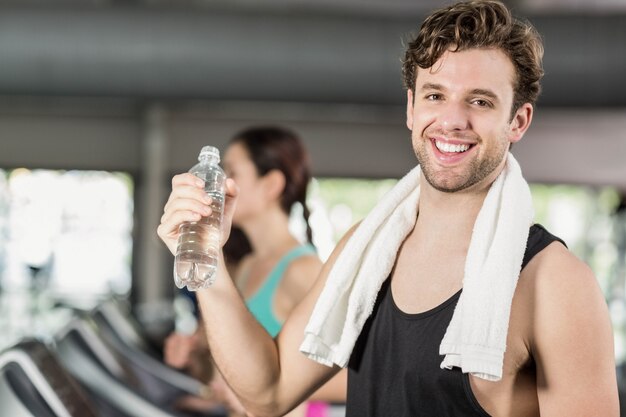 Hombre atlético bebiendo agua mientras se ejecuta en la cinta en el gimnasio