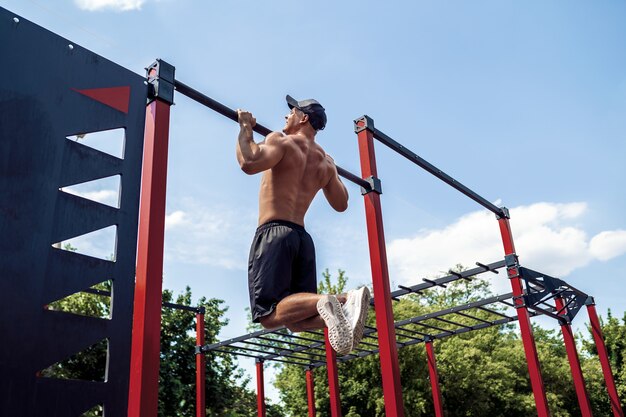 Hombre atlético brutal haciendo ejercicios de dominadas en una barra transversal.