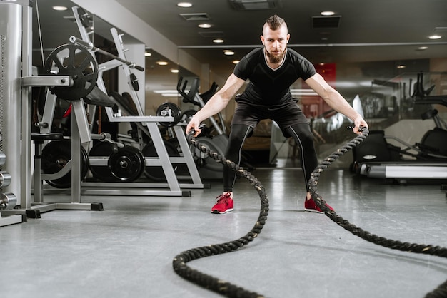 Hombre atlético con cuerda de batalla haciendo ejercicio en el gimnasio