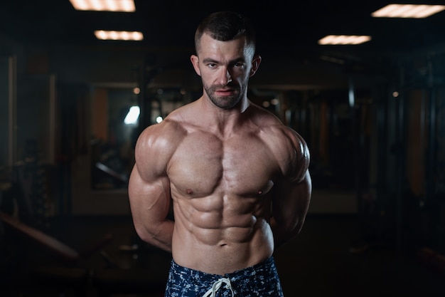 Hombre atlético con un cuerpo musculoso posa en el gimnasio, mostrando sus musculosos