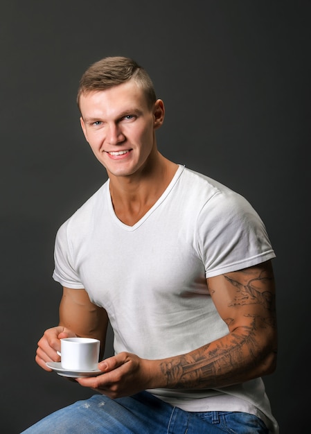 Foto hombre atlético elegante sonriendo, sosteniendo la taza de café. sentado.