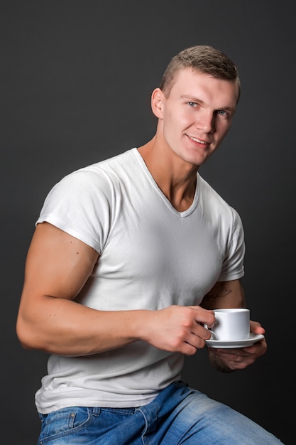 Hombre atlético elegante sonriendo, sosteniendo la taza de café. Sentado.