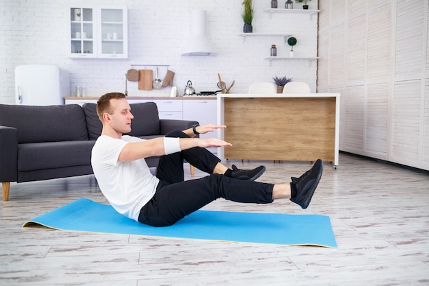 Un hombre atlético fuerte con una camiseta y haciendo ejercicios de prensa en casa en su amplio y luminoso apartamento con un interior minimalista. Hacer deporte en casa.