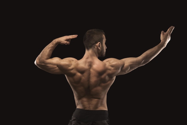 Hombre atlético fuerte que muestra grandes bíceps y cuerpo musculoso, de pie en postura competitiva culturista, vista posterior. Foto de estudio sobre fondo negro. Concepto de culturismo
