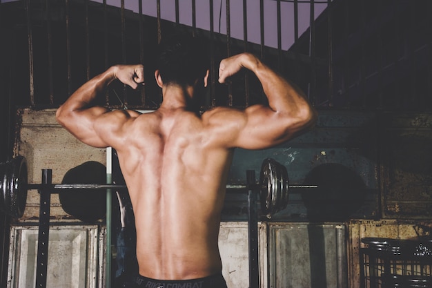 Foto hombre atlético fuerte que muestra muscel en el gimnasio local