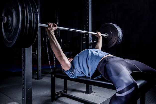 Hombre atlético en el gimnasio haciendo ejercicio en el press de banca con pesas