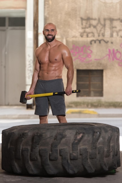 Foto hombre atlético golpea neumático en el gimnasio