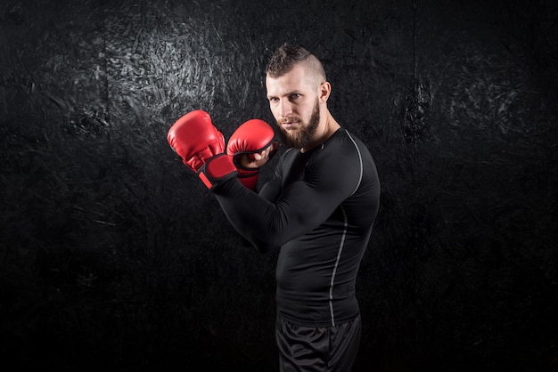 Un hombre atlético con guantes rojos de kickboxing posando y listo para pelear en el gimnasio