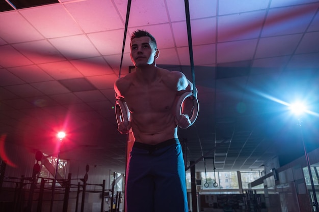 Hombre atlético haciendo ejercicio en anillos de gimnasia en luz degradada de neón azul rojo