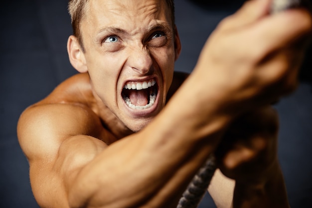 Hombre atlético joven que bombea los músculos en el gimnasio en el concepto del deporte y del cuidado de la salud del entrenamiento