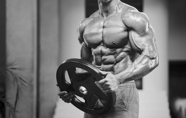 Hombre atlético joven que bombea los músculos en el gimnasio en el fondo del concepto del deporte y del cuidado de la salud del entrenamiento