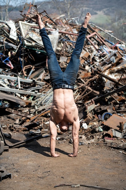 Foto hombre atlético joven que hace el pino en el depósito de chatarra industrial