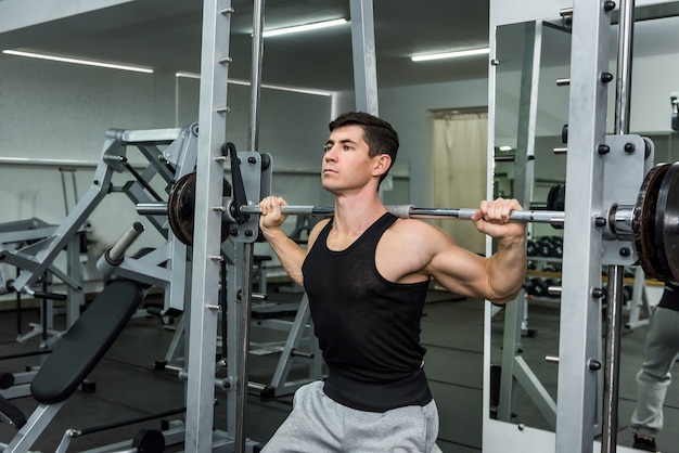 Hombre atlético levantando pesas en el gimnasio sobre los hombros