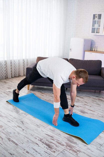 Hombre atlético musculoso en una camiseta haciendo ejercicios de calentamiento en casa. Hacer deporte en casa durante el período de cuarentena. Fitness fuera del gimnasio