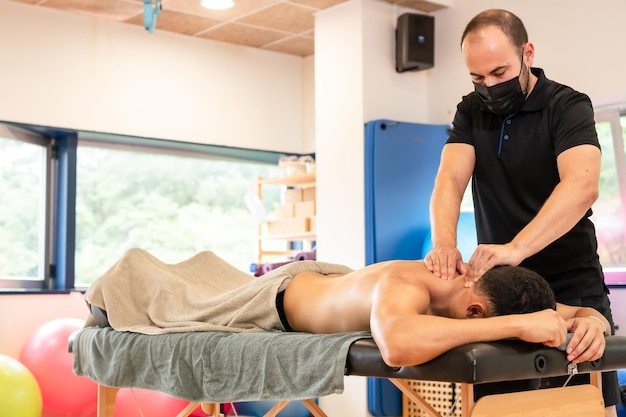 Un hombre atlético que recibe un masaje de recuperación por parte de un fisioterapeuta en una mesa de masaje terapéutico de espalda y osteopatía