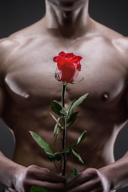 Hombre atlético con una rosa roja en la mano. Concepto de relaciones de amor y romance.