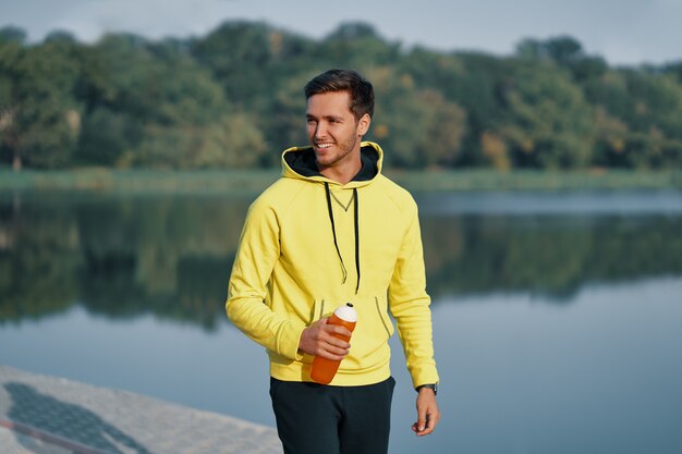 Hombre atlético sano sonriente con cuerpo en forma sosteniendo la botella